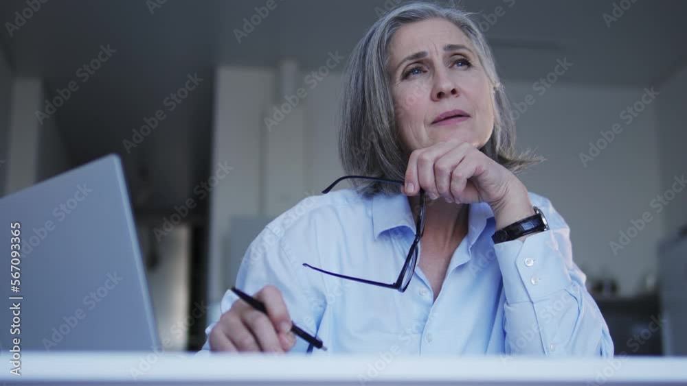 Lady boss with gray hair looking through annual report her employees sent, dissatisfied with results, taking off eyeglasses to calm painful eyes and contemplating about business improving Lady boss with gray hair looking through annual report her employees sent, dissatisfied with results, taking off eyeglasses to calm painful eyes and contemplating about business improving
