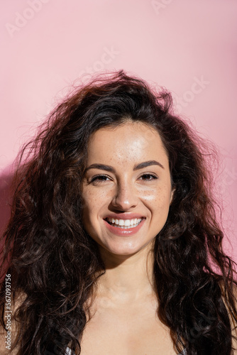 Portrait of positive woman with freckles looking at camera on pink background.