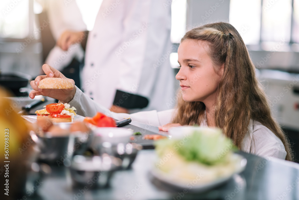 Caucasian schoolgirl concentrated to learning cooking in the kitchen with professional chef at school.