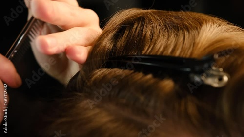 Closeup View Of barber using hair clip to fix the hair for cut and styling it. Hairdresser use pinsn hair salon. service in a modern barbershop in a dark key lightning with warm light Slow motion. photo