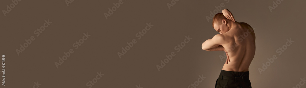 Fototapeta premium Relief, strong, muscular male back. Young man posing shirtless in pants over light brown studio background. Concept of men's health and beauty, body care, fitness. Banner. Copy space for ad, text