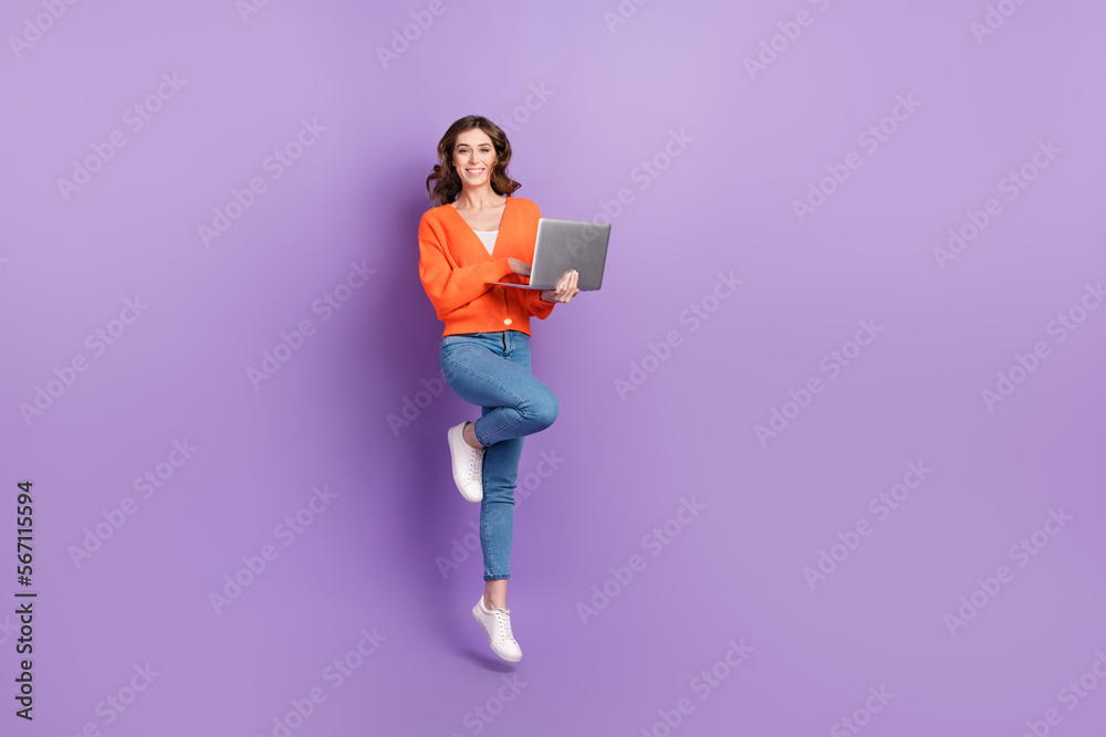 Full length photo of sweet cheerful lady wear orange cardigan jumping high working gadget empty space isolated violet color background Full length photo of sweet cheerful lady wear orange cardigan jumping high working gadget empty space isolated violet color background