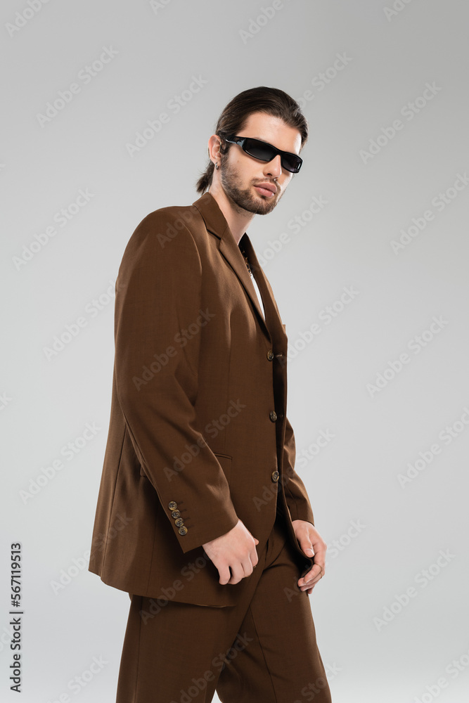 Trendy man in suit and sunglasses standing isolated on grey. Trendy man in suit and sunglasses standing isolated on grey.
