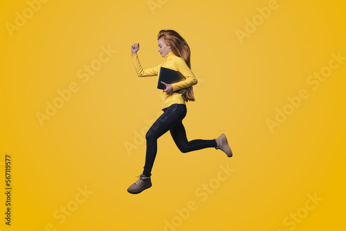 Full body of a young happy woman jumping, running holding modern device isolated on yellow color background. People lifestyle fashion concept