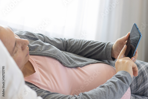 Pregnant woman in pink t-shirt using her mobile phone in the bedroom.