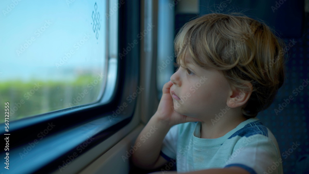 Small child leaning on train window staring at landscape passing by. One boy on moving transportation Small child leaning on train window staring at landscape passing by. One boy on moving transportation