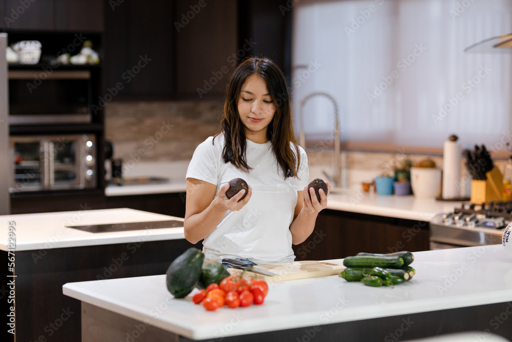 Hispanic woman preparing healthy food - young woman holding avocados for her healthy meal