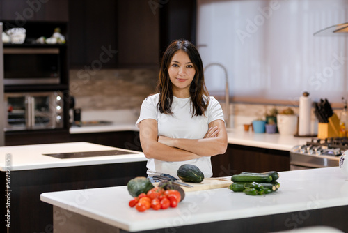 Young hispanic woman proud of her healthy food - woman with vegetables in her kitchen ready to prepare vegan food