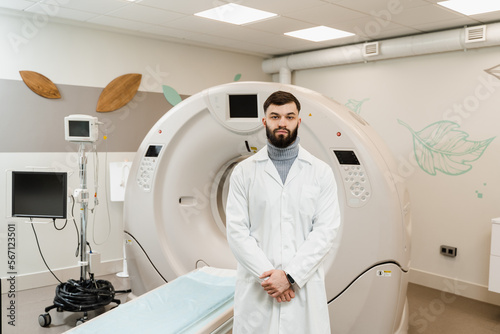 Man doctor in CT scan computed tomography room in medical clinic. Handsome bearded doctor in medical robe with computed tomograph for obtain detailed internal images of the body of patient.