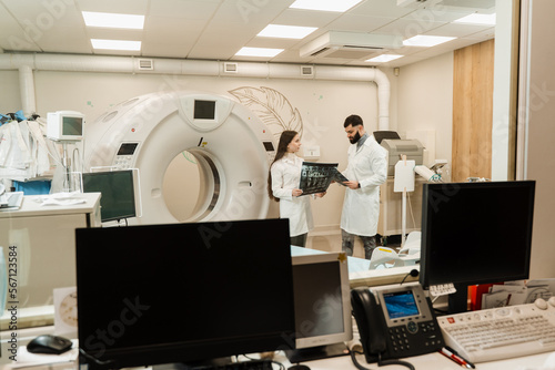 Two doctors discussing x-rays after CT scan of patient abdomen. CT Computed tomography scan procedure to obtain detailed internal images of body and research on tumors in head, brain, and spine.