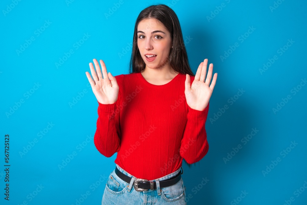 young brunette girl wearing red T-shirt against blue wall Moving away hands palms showing refusal and denial with afraid and disgusting expression. Stop and forbidden. young brunette girl wearing red T-shirt against blue wall Moving away hands palms showing refusal and denial with afraid and disgusting expression. Stop and forbidden.