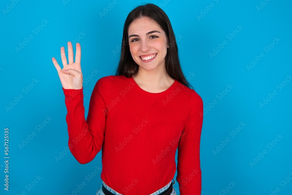 young brunette girl wearing red T-shirt against blue wall showing and pointing up with fingers number four while smiling confident and happy. young brunette girl wearing red T-shirt against blue wall showing and pointing up with fingers number four while smiling confident and happy.
