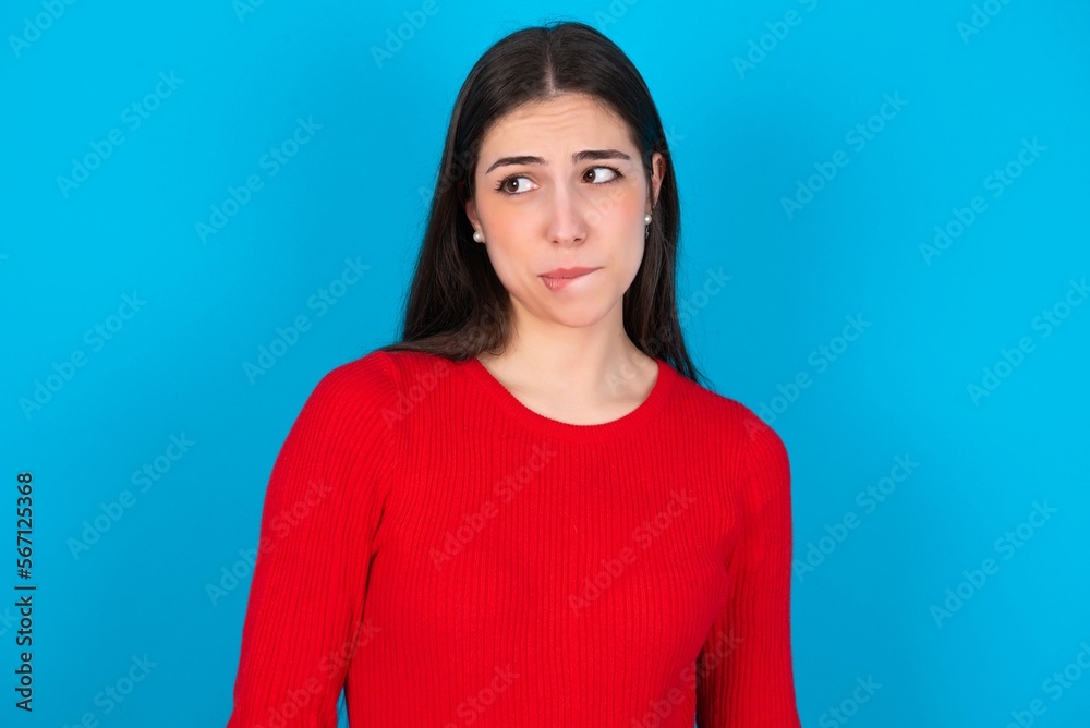 young brunette girl wearing red T-shirt against blue wall making grimace and crazy face, screaming out of control, funny lunatic expressing freedom and wild. young brunette girl wearing red T-shirt against blue wall making grimace and crazy face, screaming out of control, funny lunatic expressing freedom and wild.