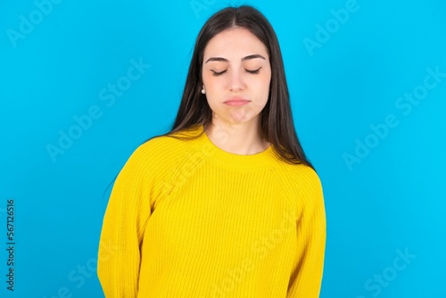 young brunette girl wearing yellow knitted sweater against blue wall depressed and worry for distress  crying angry and afraid. Sad expression.