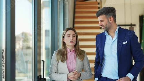 Beautiful businesswoman entrepreneur walking and talking with handsome businessman in blue suit discussing new project at modern workplace near big windows. Corporate business collaboration concept