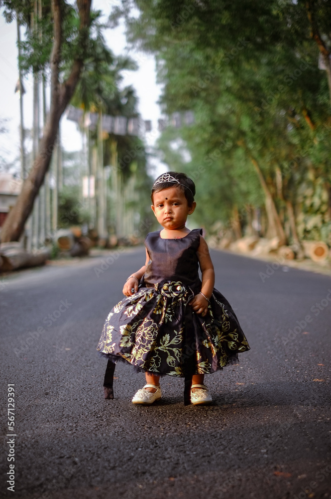 South asian cute little adorable baby girl walking on a rural road wearing colourful princess dress