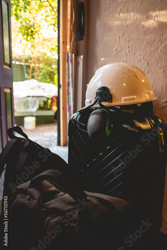 PPE (white safety helmet with attached earmuffs) over  a black suitcase and bags at the door in the day photo