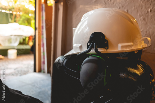 PPE (white safety helmet with attached earmuffs) over  a black suitcase and bags at the door in the day