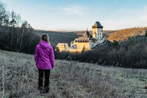 Woman tourist outdoors looking at beautiful gothic Royal Karlstejn Castle Czech Republic.Most popular Czech castle at sunset.Travel romantic scenery leisure activity on sunny day.Happy hiking female