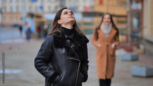 Fotografie A friend comes up from behind her waiting girlfriend on a city street