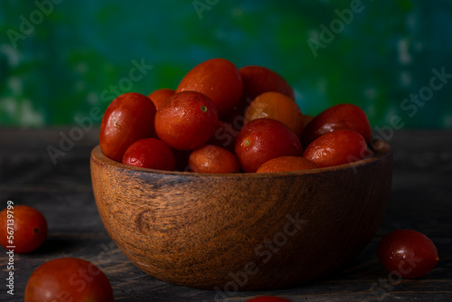 Tomates rojos en cuenco de madera sobre mesa de madera y fondo verde