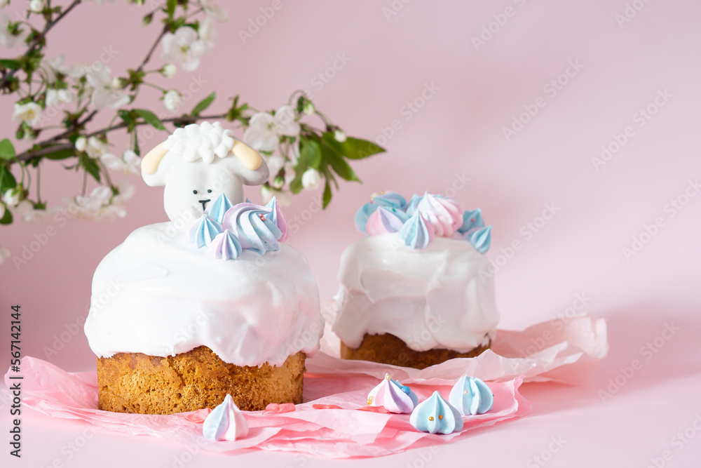 Easter cake with white icing and blue meringues Easter decorative lamb on a pink background with spring cherry blossoms and copy space. Easter Ukraine orthodox sweet bread. Easter card concept. Easter cake with white icing and blue meringues Easter decorative lamb on a pink background with spring cherry blossoms and copy space. Easter Ukraine orthodox sweet bread. Easter card concept.