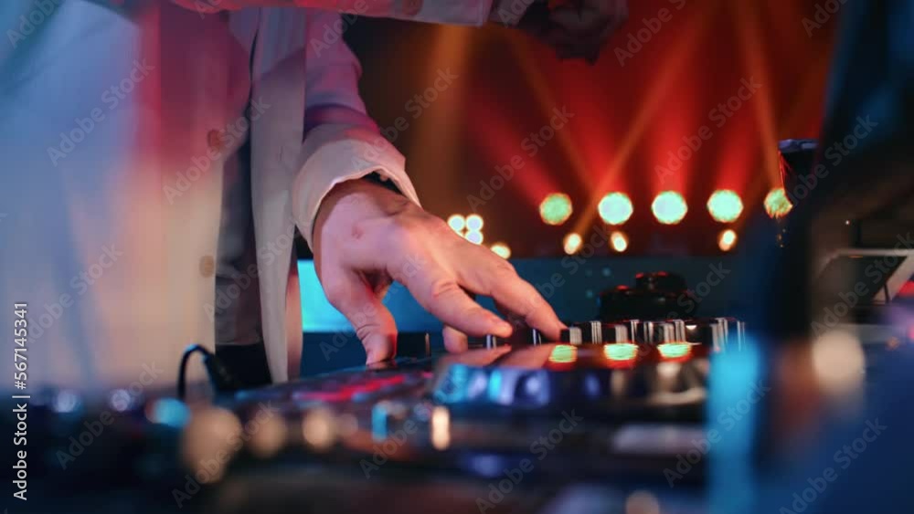 DJ hands mixing music turntable console control panel at illuminated nightclub party closeup
