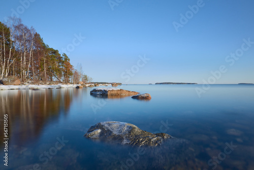 Before sunset at the end of winter in Uutela near Helsinki big alone stone against a backdrop of clear blue water and coastline.