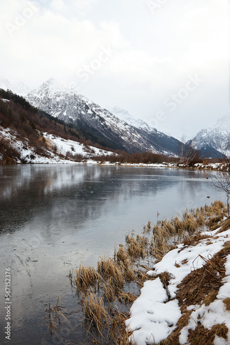winter mountain lake in snow, in background of mountain, landscape pond with ice on water