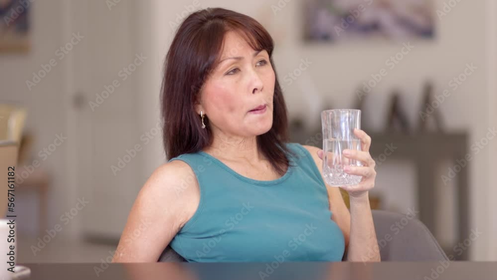 Attractive mature woman relaxing drinking glass of water looking around sitting in leisure home living room Attractive mature woman relaxing drinking glass of water looking around sitting in leisure home living room