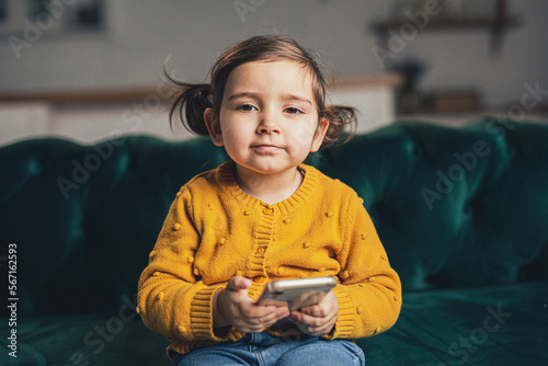 Little girl using technology. baby sitting on the sofa and play with mobile phone
