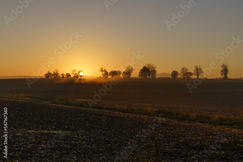 Beautiful sunrise over the mountains in the area of still shaded farmland