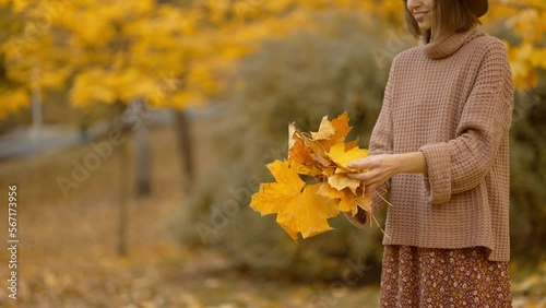 slow motion autumn portrait of attractive smiling woman wearing in brown dress, sweater and hat. girl holds yellow leaves, playfuly looking at camera and throws leaves up photo