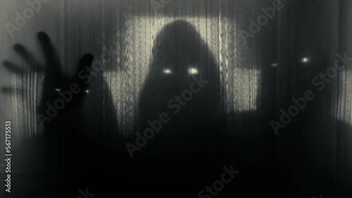 Silhouettes of three people in hoods with glowing eyes behind a transparent curtain, raising their heads and pulling out their hands. Concept of demons, paranormality, ghosts. 4k video 60 fps. photo