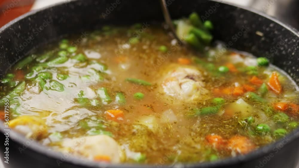 Homemade chicken vegetable soup cooking, close up view of chef cooking vegan healthy soup in big pan pot. Homemade chicken vegetable soup cooking, close up view of chef cooking vegan healthy soup in big pan pot.