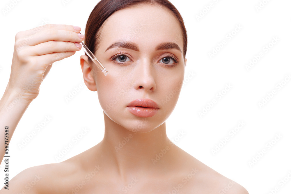 Portrait of an attractive young brunette woman with bare shoulders holding a serum pipette near her face on a white background. The concept of make-up, cosmetic procedures.