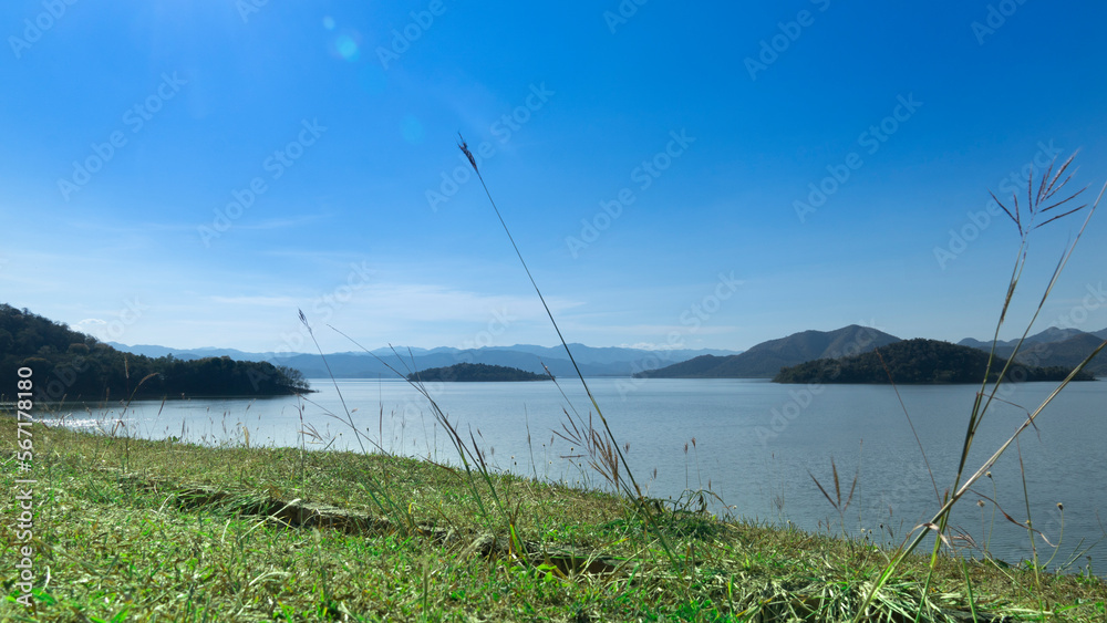 Front view of green grass. and background landscape of island on the reservoir under blue sky. At Kaeng Krachan Reservoir, Phetchaburi, Thailand. Front view of green grass. and background landscape of island on the reservoir under blue sky. At Kaeng Krachan Reservoir, Phetchaburi, Thailand.
