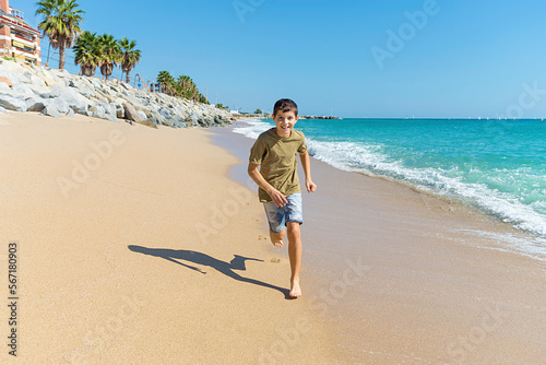 Front view of young boy barefoot running on beach while smiling