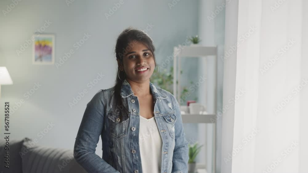 Portrait of positive Indian woman looking in camera with dazzling smile on face. Young female person shows friendly attitude standing near window Portrait of positive Indian woman looking in camera with dazzling smile on face. Young female person shows friendly attitude standing near window