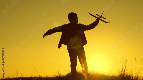 Child boy aviator plays with toy plane in park in sunset. Child wants to become an astronaut. Children play with toy plane. Teenager dreams of flying, becoming pilot. Boy dreams of flying, traveling