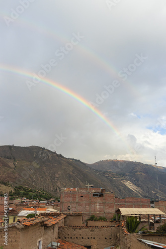 Double rainbow in the afternoon, with view of some adobe and brick houses, mountains and sky, taken in the afternoon in Caraz.
