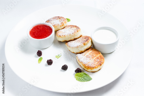 Cottage cheese pancakes, traditional Ukrainian syrniki served with sour cream and raspberry jam on white plate, healthy breakfast or brunch.