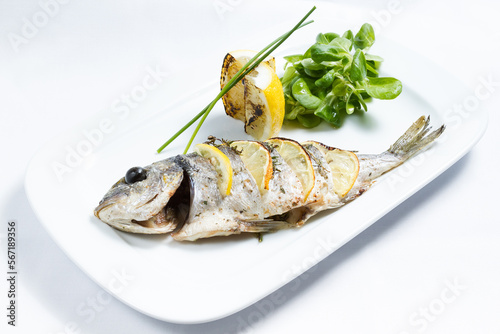 Grilled dorado fish, lemon, mache salad on white plate.