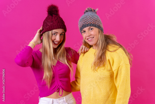 Two blonde caucasian women in wool hats on a pink background, portrait looking
