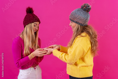 Two young blonde caucasian women giving a present on a birthday on an isolated on a pink background