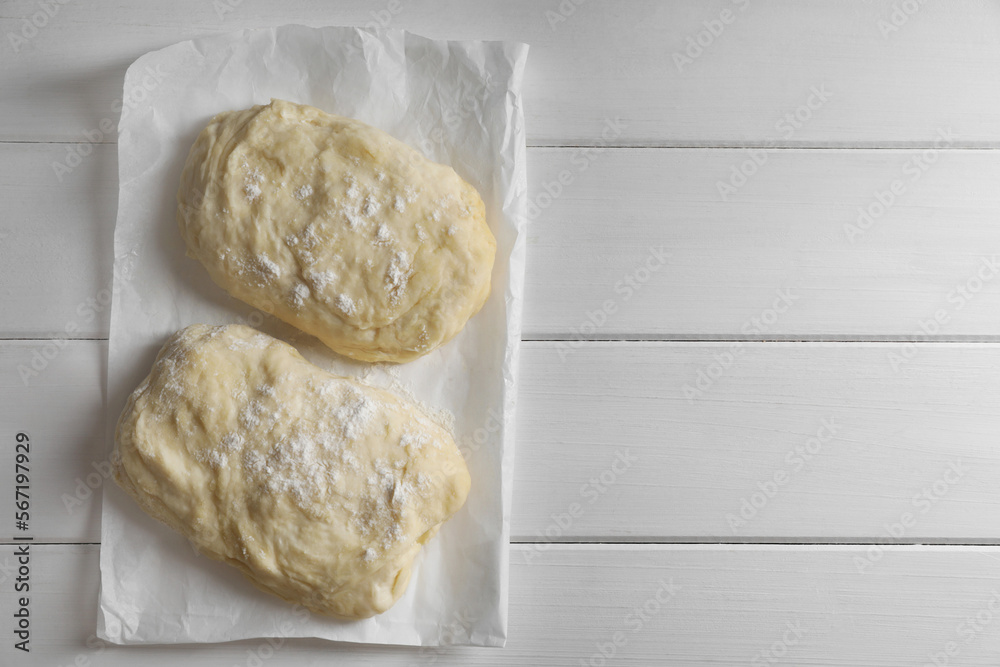 Raw dough and flour on white wooden table, top view with space for text. Cooking ciabatta