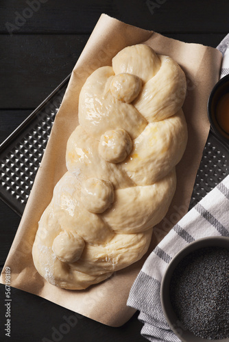 Raw braided bread and poppy seeds on black wooden table, flat lay. Traditional Shabbat challah photo