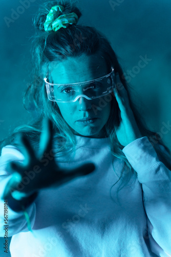 Woman with futuristic glasses gesturing against a blue background, illuminated glasses