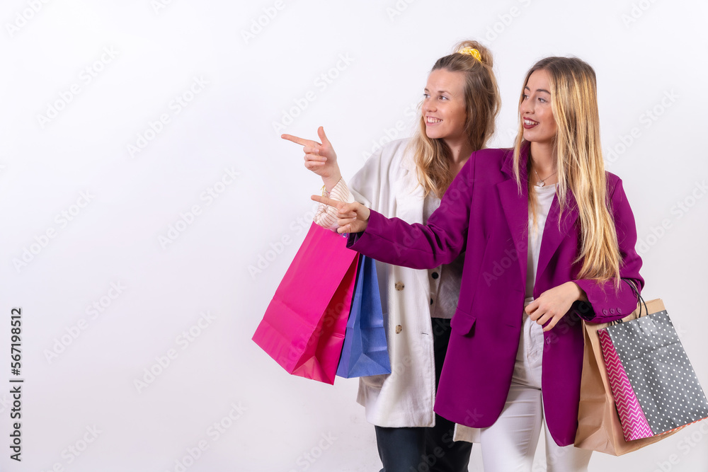 Two young blonde caucasian women, friends concept shopping in the sales pointing, paper bags