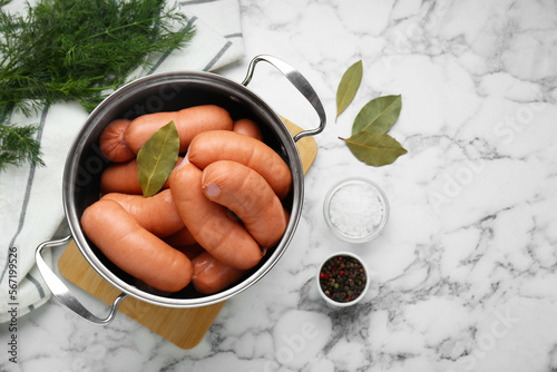 Pan of delicious sausages, dill, bay leaf, pepper and salt on white marble table, flat lay. Space for text photo